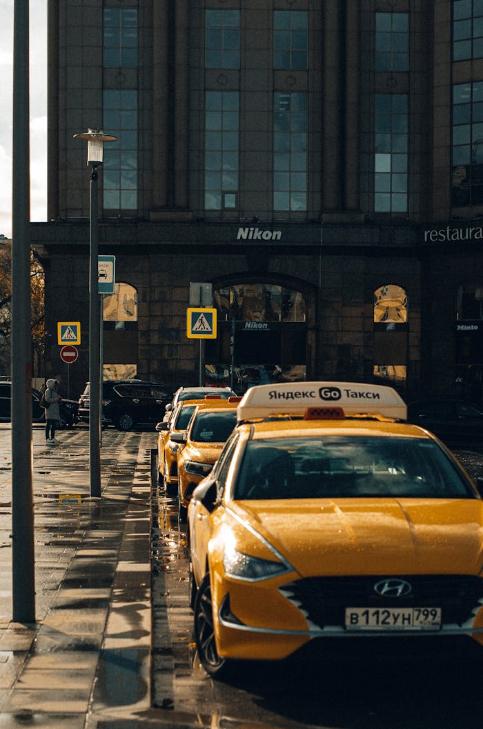 Urban scene featuring parked yellow taxis on a city street in front of a building on a rainy day.