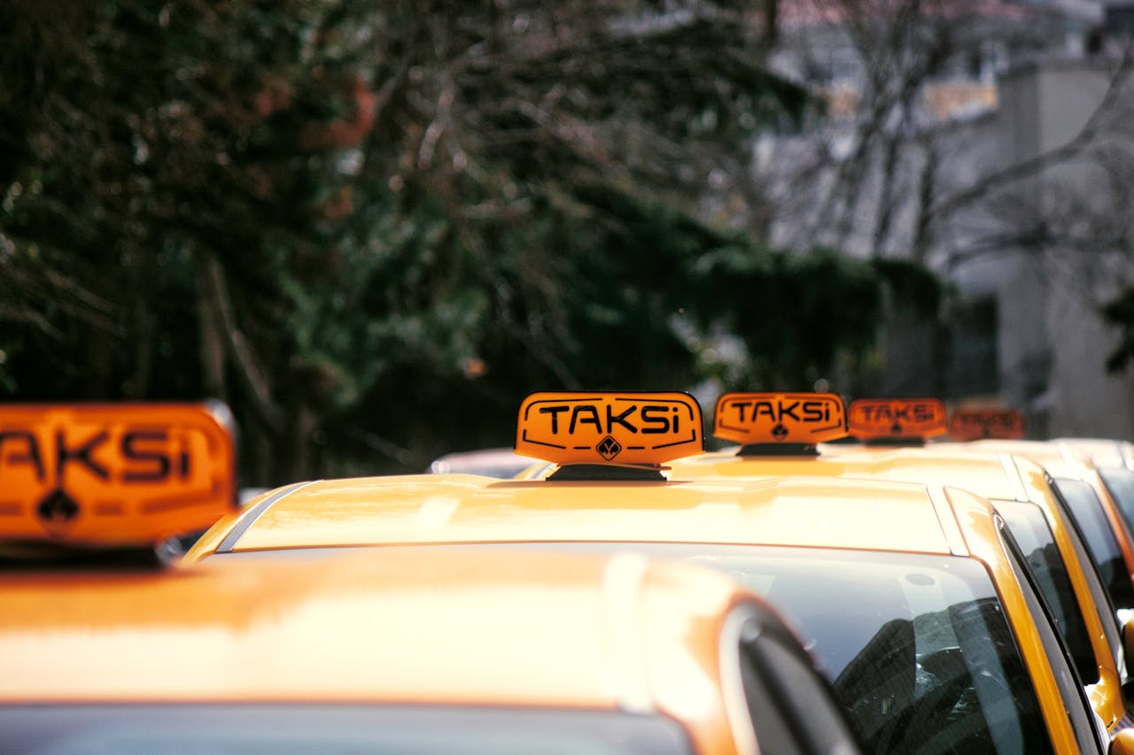 gallery-3 A row of yellow taxis with 'Taksi' signs parked on a city street in daylight.