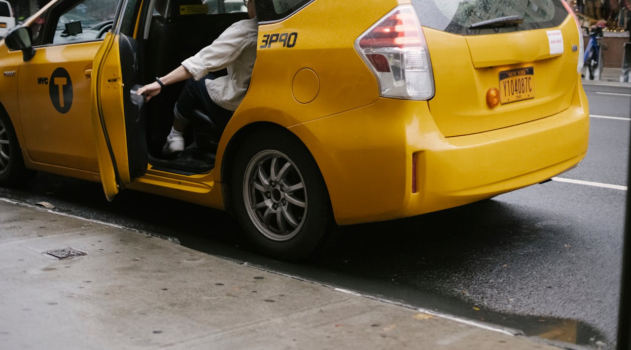 gallery-2 Unrecognizable passenger closing door of yellow cab with logo and headlight parked on asphalt road near pavement on street in city